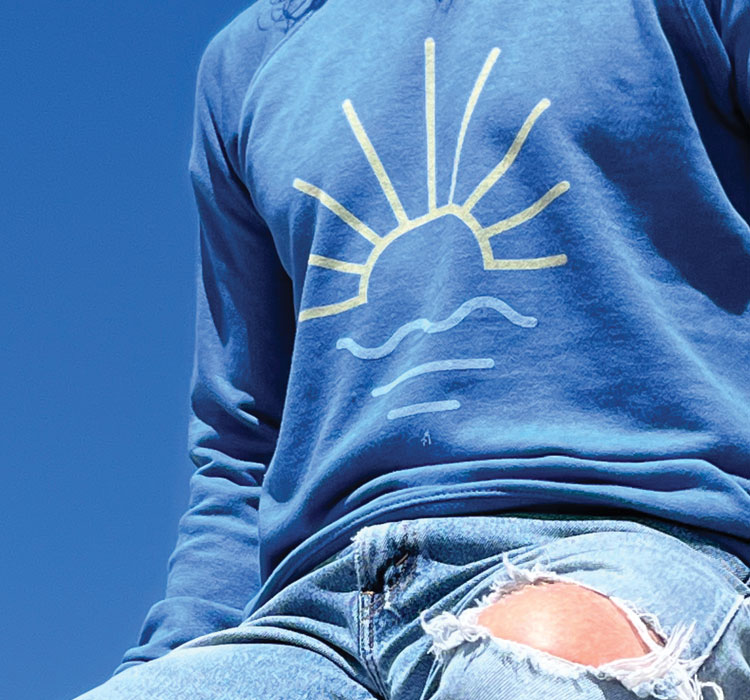 Person wearing blue t-shirt with sun/wave logo in a park