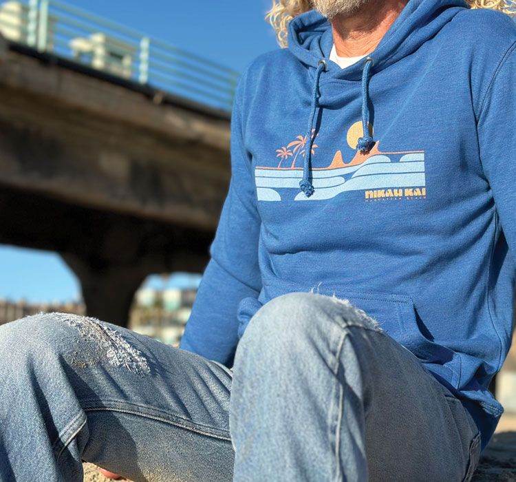 Blue hoodie with sunset/wave design near a pier