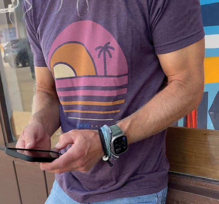 Back view of blue t-shirt with Nikau Kai logo and palm trees