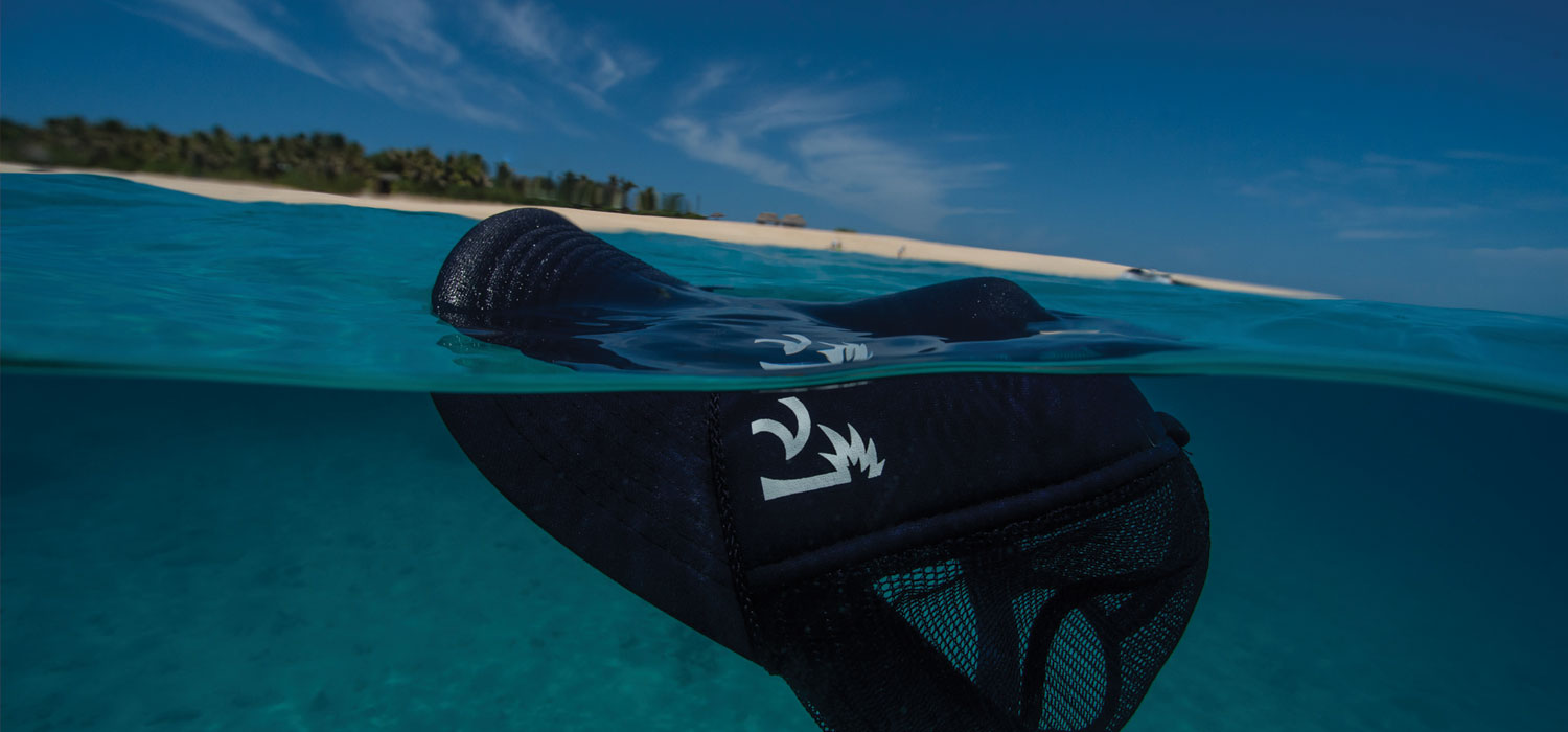 Underwater view of a Nikau Kai hat partially submerged in clear water with beach above